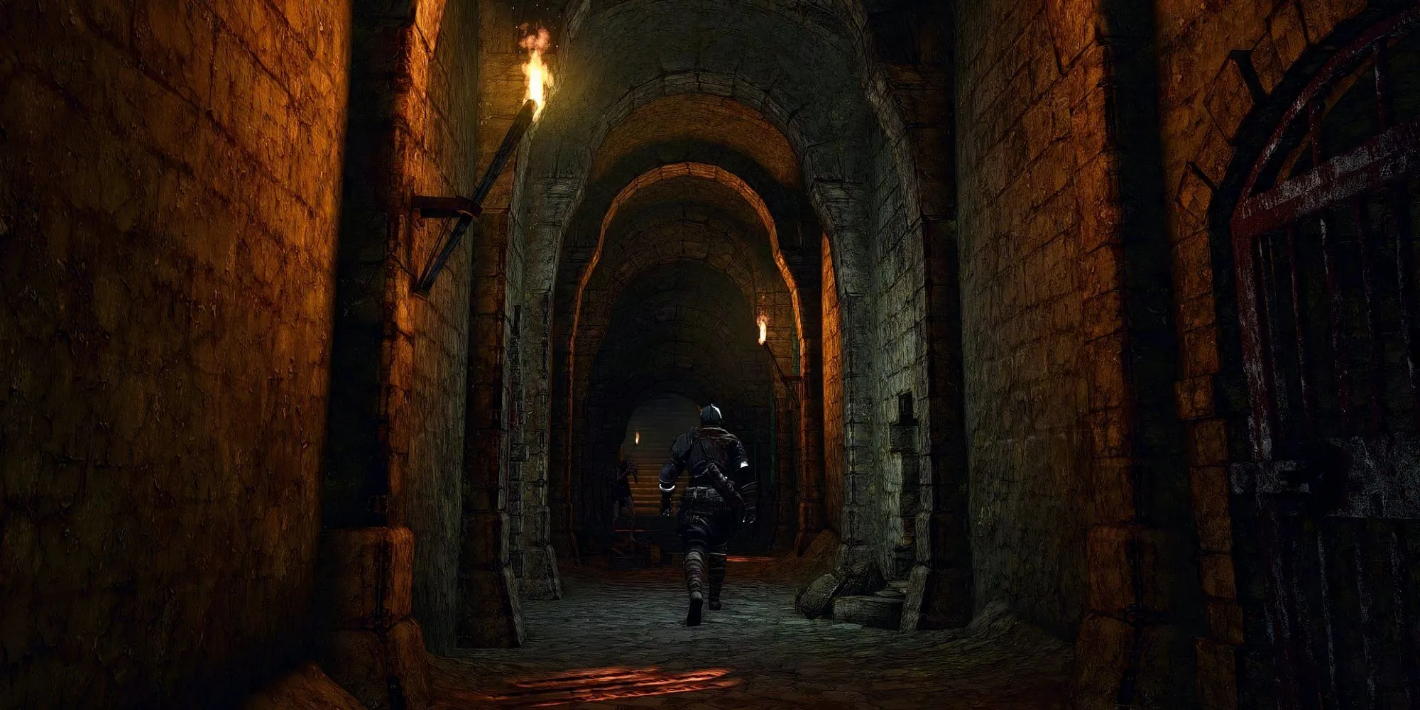 Hiệp sĩ Oscar nằm hấp hối trong xà lim tại Undead Asylum, Dark Souls, phía xa là con quỷ Asylum Demon