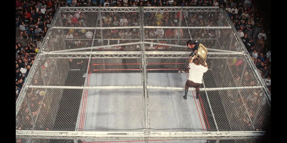 Mankind (Mick Foley) chuẩn bị bị ném từ đỉnh lồng Hell in a Cell xuống bàn bình luận viên